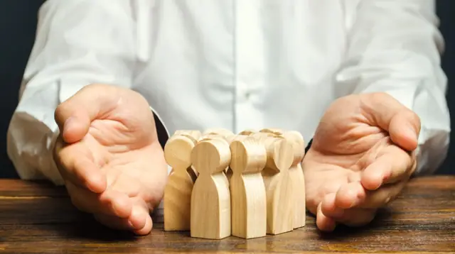 Mãos protegendo miniaturas de madeira de uma família