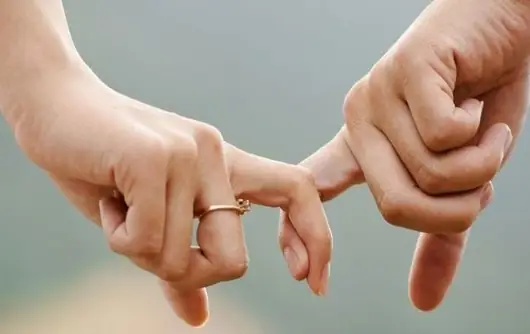 Mãos de um casal entrelaçadas pelo dedo mínimo